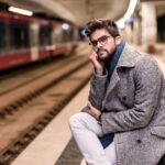 Man in gray coat sitting at train station.