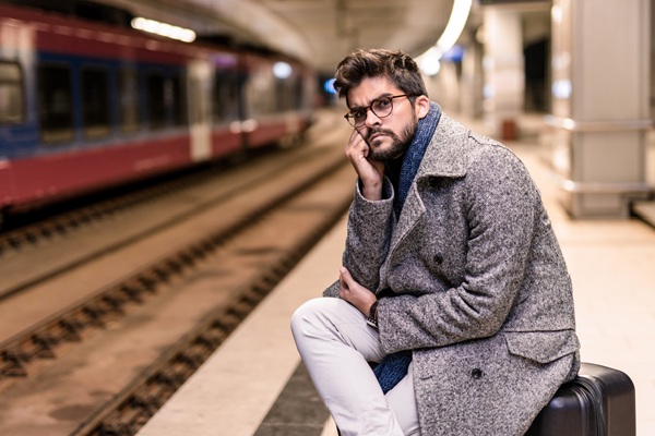 Man in gray coat sitting at train station.