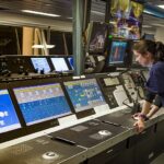 Vrouw werkt in scheepsbrug met computerschermen.
