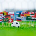 Voetbal met internationale vlaggen op grasveld.