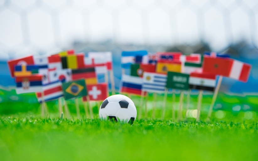 Voetbal met internationale vlaggen op grasveld.