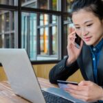 Vrouw telefoneert met laptop en creditcard