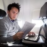 Man werkt op laptop in vliegtuigstoel
