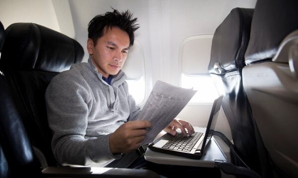 Man werkt op laptop in vliegtuigstoel