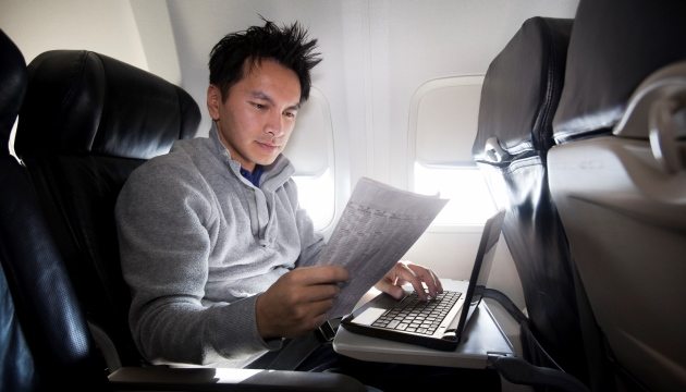 Man werkt op laptop in vliegtuigstoel