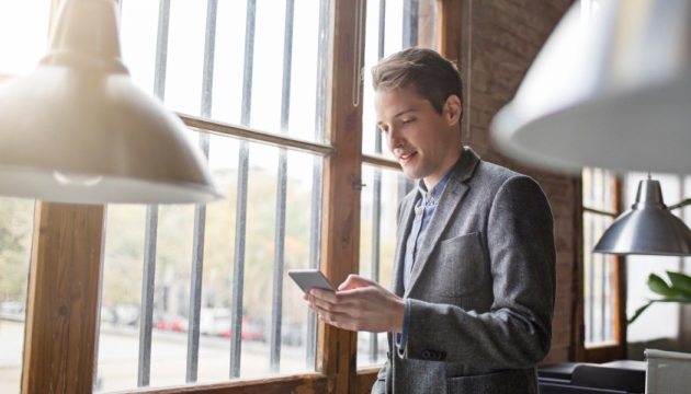 Man bij raam met smartphone, moderne kantoorruimte