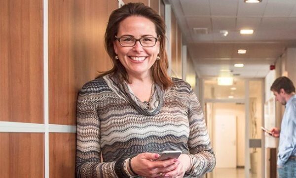 Vrouw met telefoon in kantoorhal lachend.