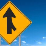 Verkeersbord samenvoegende rijstroken onder blauwe hemel