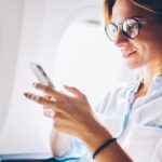 Vrouw met telefoon in vliegtuig, glimlachend.