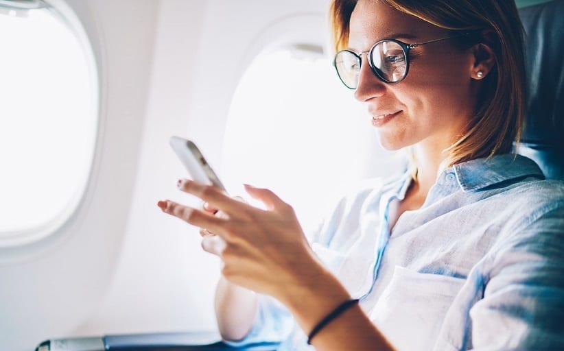 Vrouw met telefoon in vliegtuig, glimlachend.