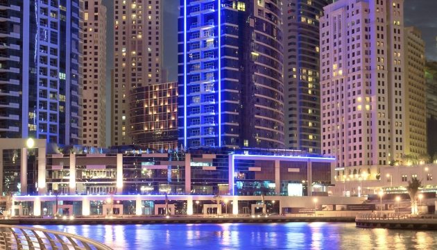 Verlichte moderne skyline met hoge gebouwen en water.