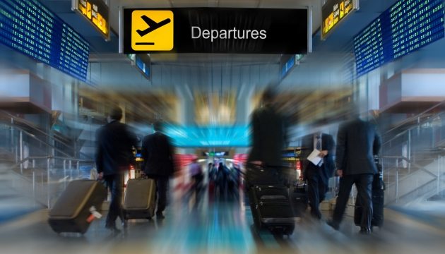 Reizigers op luchthaven met vertrekscherm op achtergrond.