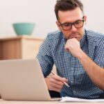 Man werkt geconcentreerd op laptop met koffie en croissant.