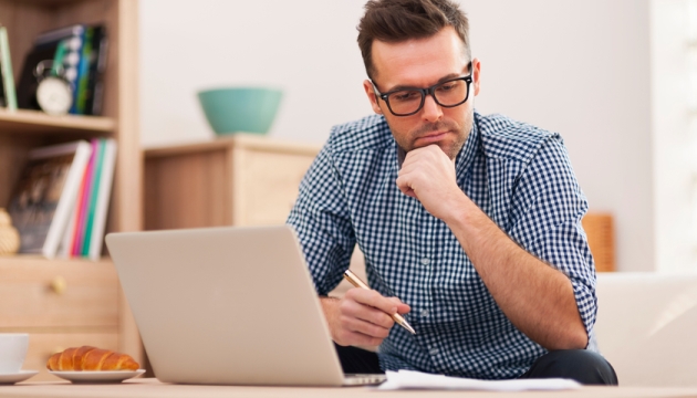 Man werkt geconcentreerd op laptop met koffie en croissant.