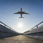 Vliegtuig vliegt over brug in zonlicht.