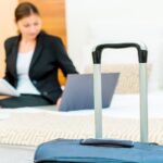 Vrouw in hotelkamer met koffer en laptop.