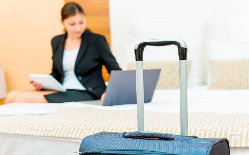 Vrouw in hotelkamer met koffer en laptop.