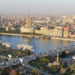 Panorama van drukke stad met rivier en brug.