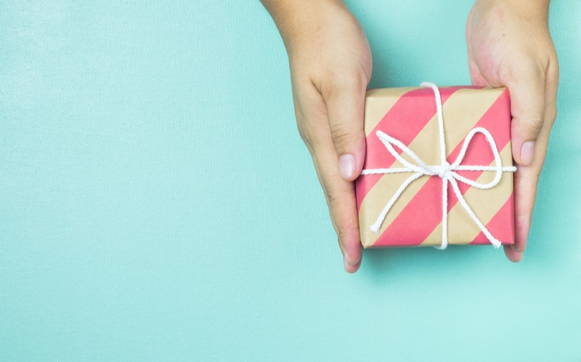 Handen met ingepakt cadeau op blauw achtergrond.