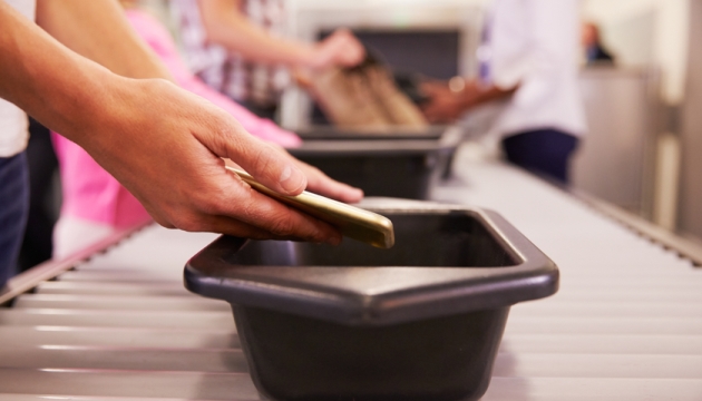 Persoon legt telefoon op bagageband op luchthaven.