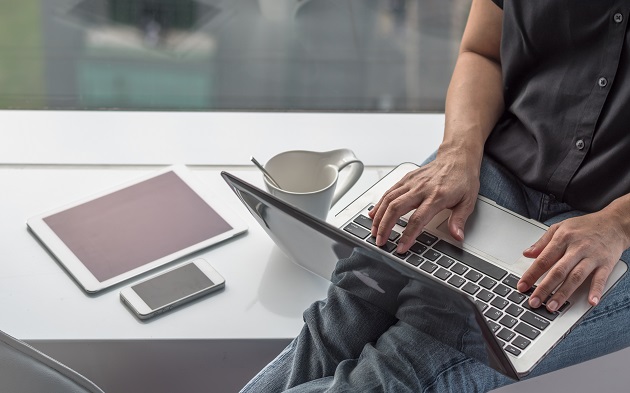 Pers werkt op laptop bij raam met tablet.