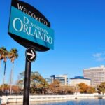 Welkomstbord bij Downtown Orlando met stad op achtergrond.