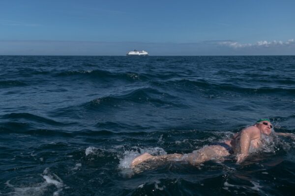 Zwemmer in zee met veerboot op de achtergrond