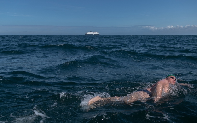 Zwemmer in zee met veerboot op de achtergrond