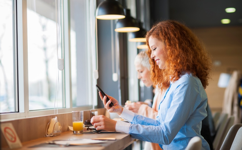 Vrouw drinkt sap in café, gebruikt mobiele telefoon.