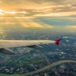 Vleugel van vliegtuig boven stad in zonsondergang.