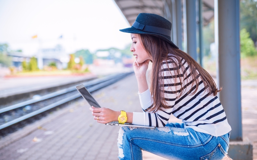 Vrouw leest op tablet bij treinperron.