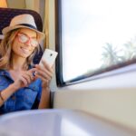 Vrouw in trein met telefoon en hoed.