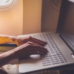 Persoon typt op laptop in vliegtuig.