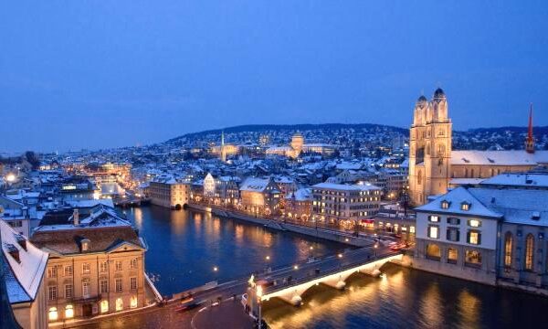 Sneeuwachtig stadslandschap met verlichte brug en rivier.