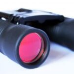 Zwarte verrekijker met rode lenzen op witte achtergrond.