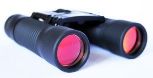 Zwarte verrekijker met rode lenzen op witte achtergrond.