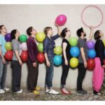 Mensen rij met kleurrijke ballonnen aan muur.