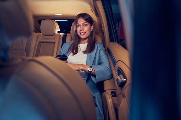 Woman holding coffee cup in car backseat.