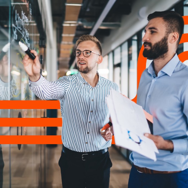 Two coworkers review diagrams on a glass office board
