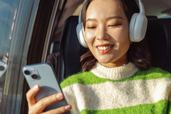 Woman wearing headphones smiling at smartphone on train