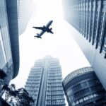 Airplane flying over tall skyscrapers in city.