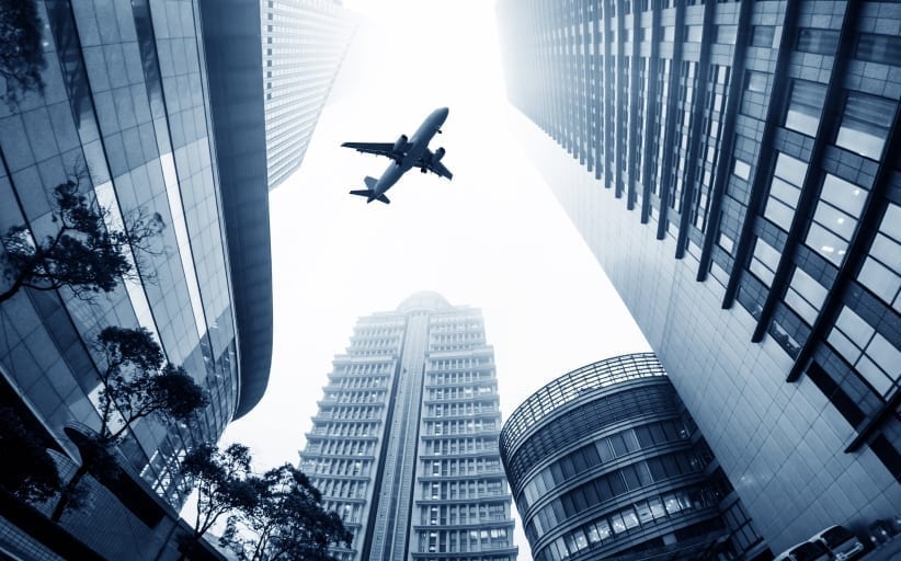 Airplane flying over tall skyscrapers in city.