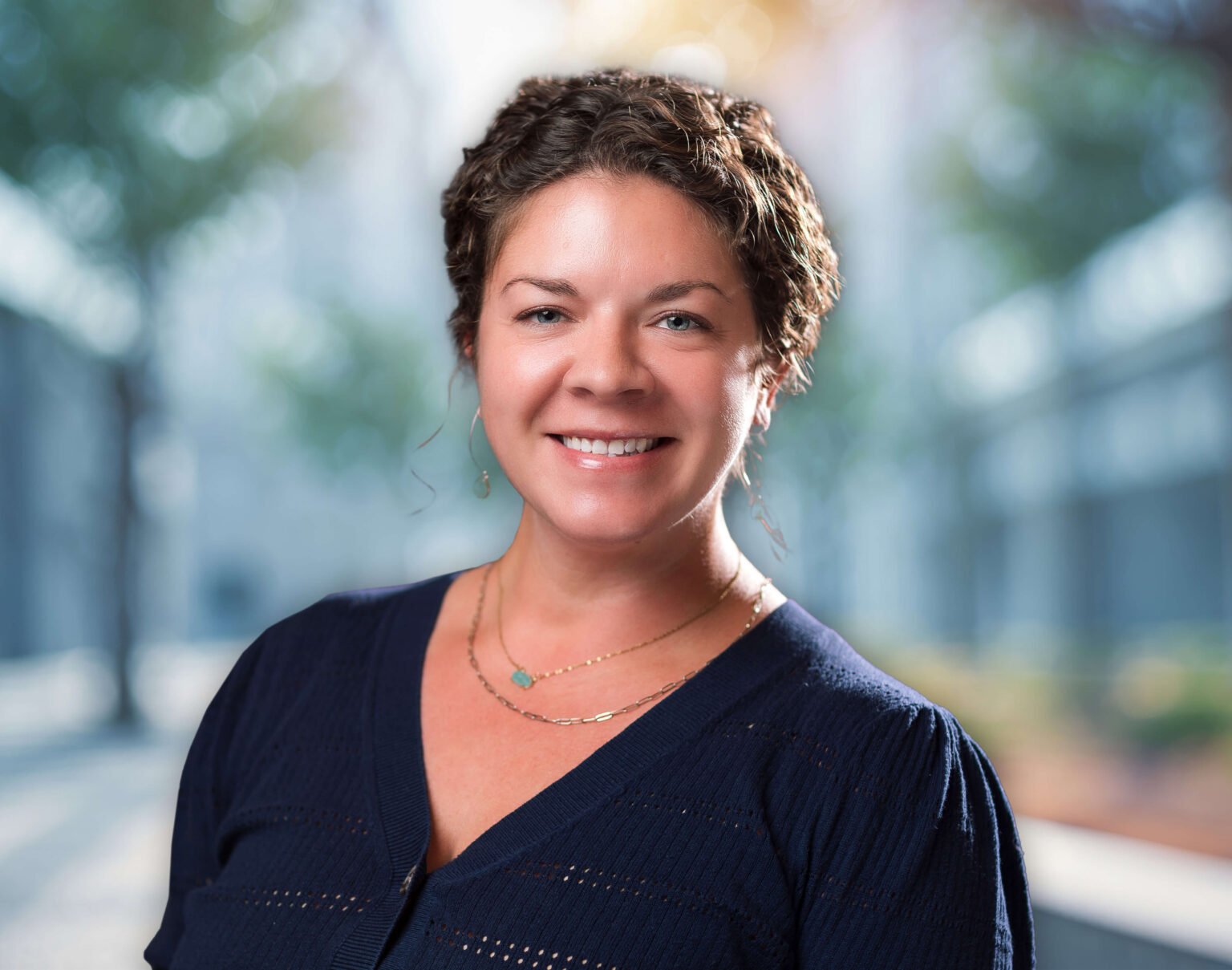 Smiling woman in navy cardigan wearing layered necklaces