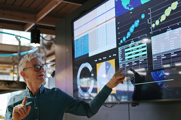 Man pointing at data dashboards on large monitor