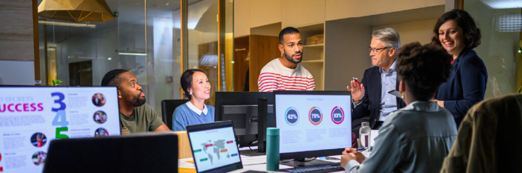Team meeting discussing data on office monitors