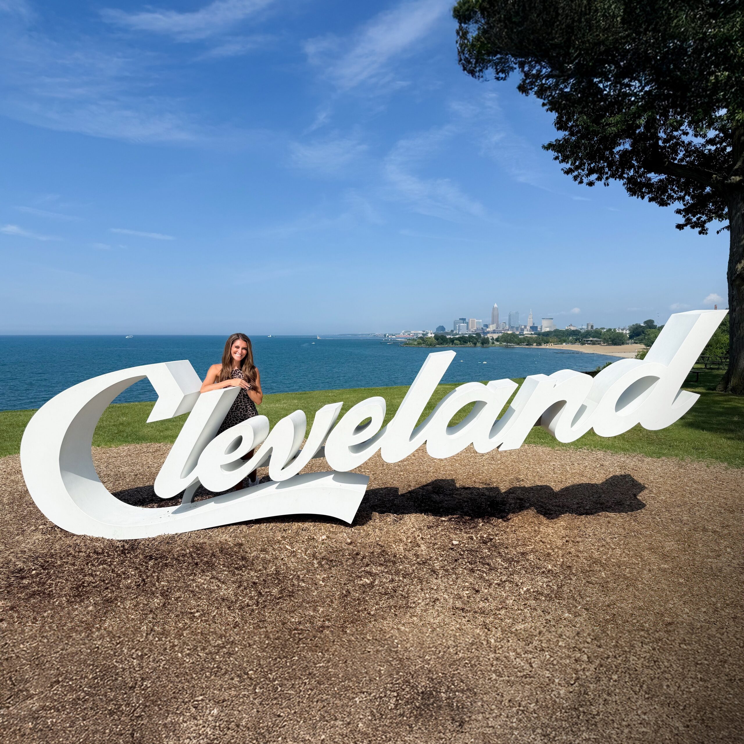 Woman standing by Cleveland sign, city skyline.