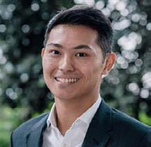 Smiling person in a suit with blurred background.