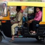 Yellow auto rickshaw with passenger on city street.