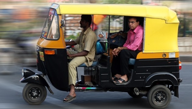 Yellow auto rickshaw with passenger on city street.