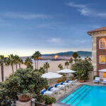 Beachfront hotel with pool and ocean view at sunset.
